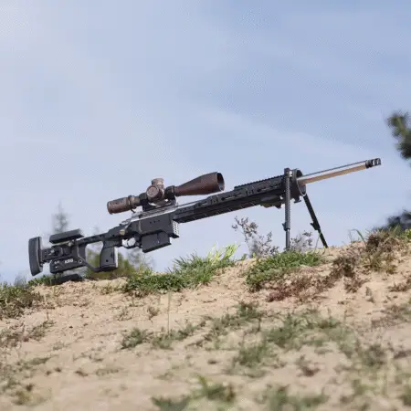 A rifle in a C-4 Chassis. The rifle is on a sandy hill and is using an Elite Iron bipod